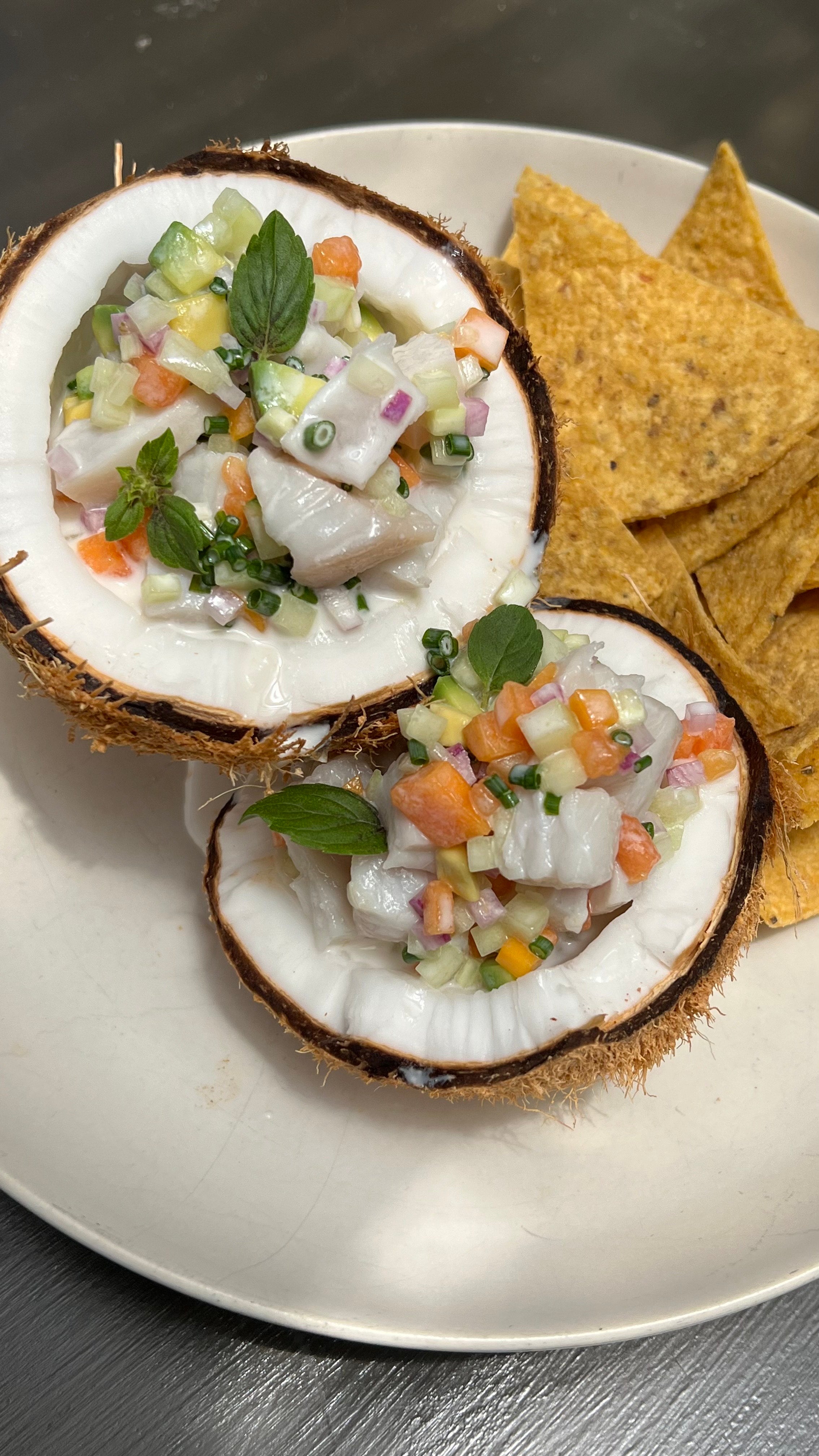Fresh Coconut Poisson Cru combines fresh, citrus-cured fish and silky coconut milk with fresh papaya and cucumber. Served with MASA Chips. 