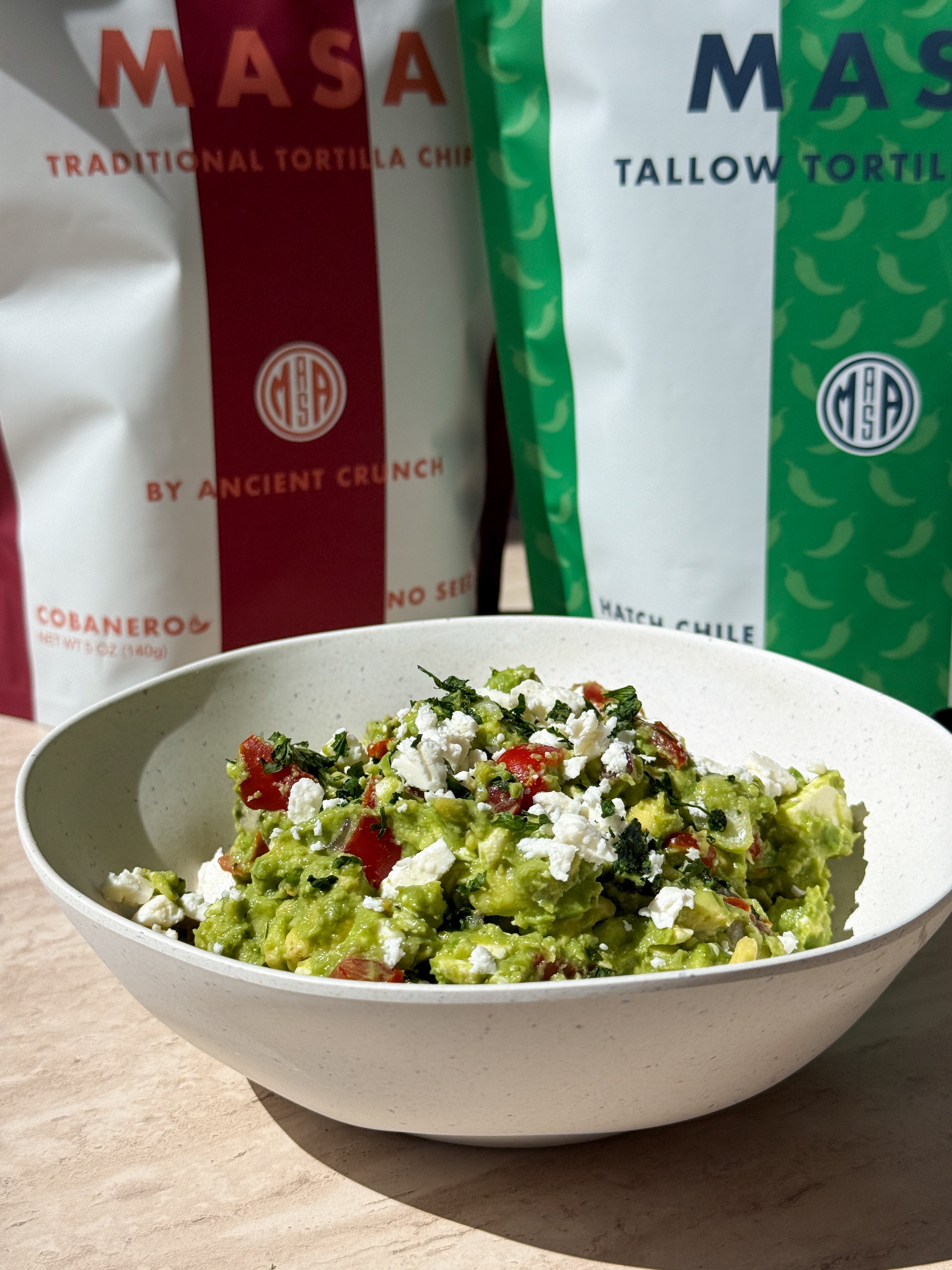 This vibrant avocado dip combines bright lemon juice, sweet tomatoes, and salty feta cheese, served with crispy MASA chips for the ultimate chunky scoop.